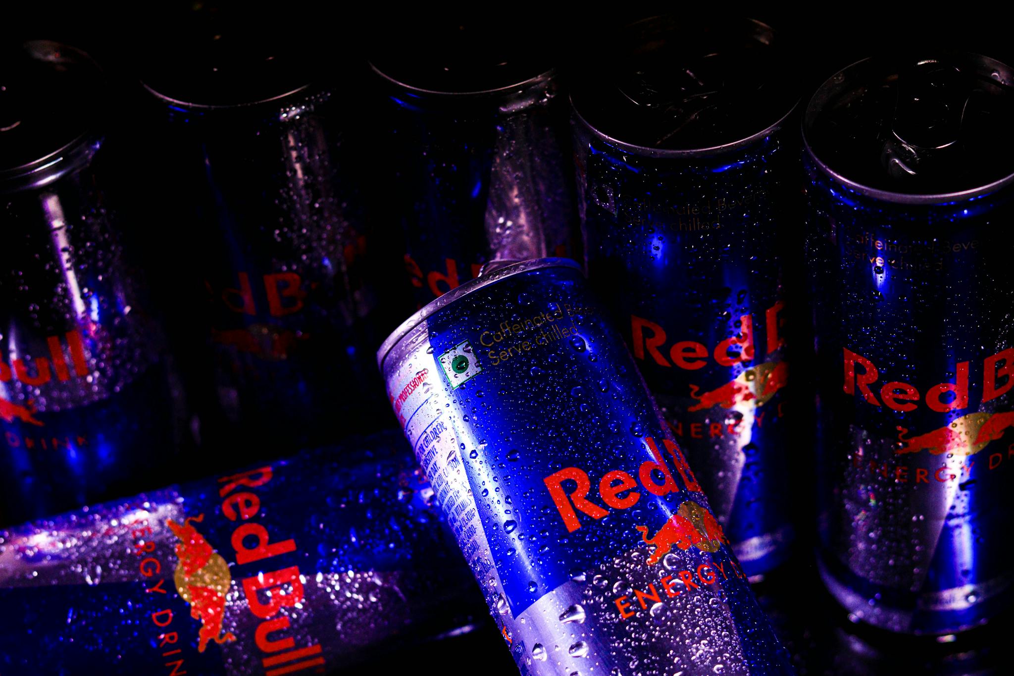 Close-up of Red Bull energy drink cans with refreshing water droplets, showcasing branding.