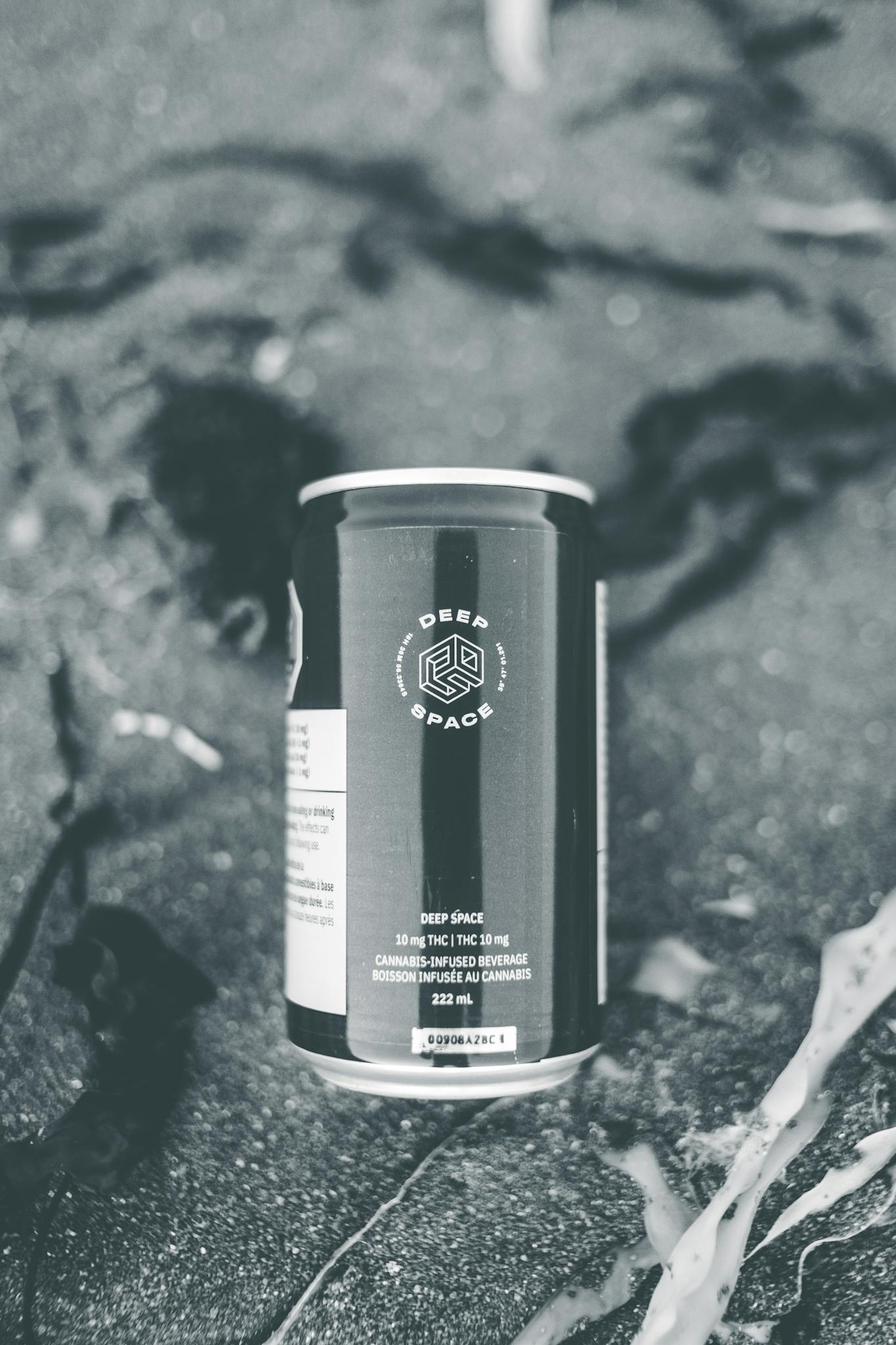 Monochromatic image of a beverage can on a sandy surface with plant life.